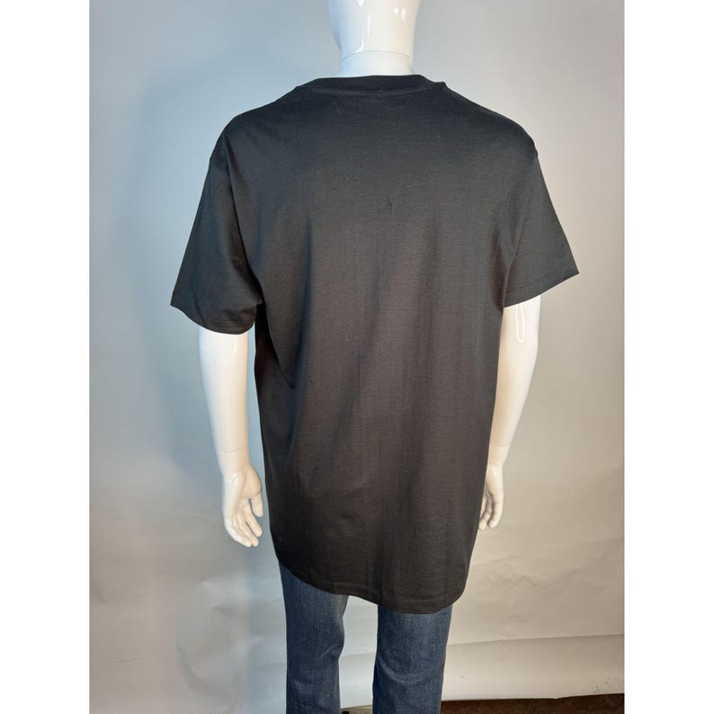 May include: A black short-sleeved t-shirt on a mannequin. The shirt is a solid black color and appears to be made of a soft material. The mannequin is wearing blue jeans.
