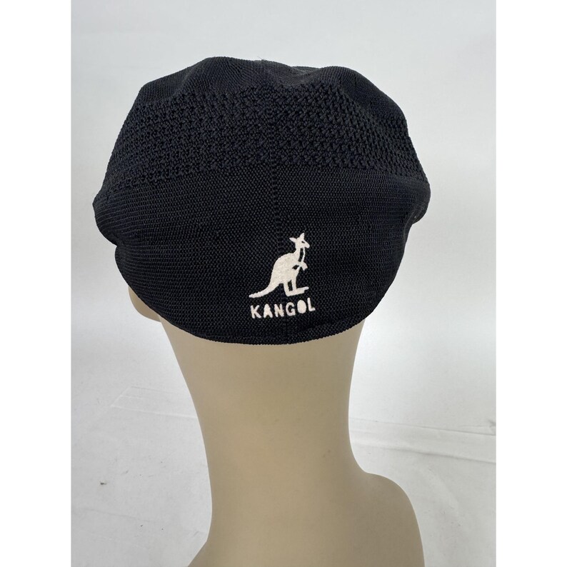 May include: Black Kangol hat with a white kangaroo logo. The hat is made of a textured material and has a rounded crown. The logo and text are embroidered on the back of the hat.