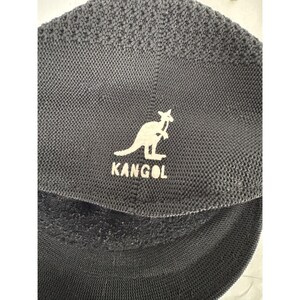 May include: Dark gray Kangol hat with a white kangaroo logo and the brand name. The hat has a textured knit pattern and a curved brim. The logo is centered on the front of the hat.