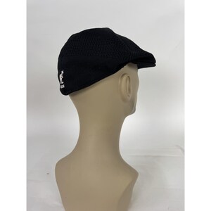 May include: Black newsboy cap with a textured knit design. The cap features a small white kangaroo logo on the side. This classic style hat is a versatile accessory.