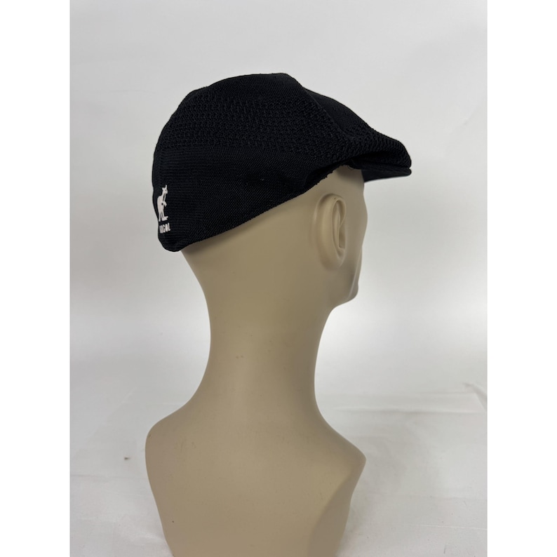 May include: Black newsboy cap with a textured knit design. The cap features a small white kangaroo logo on the side. This classic style hat is a versatile accessory.