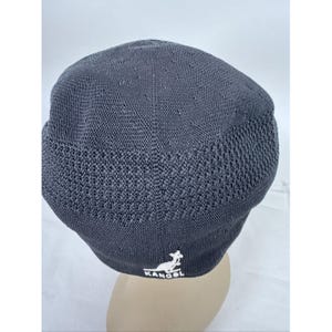 May include: A charcoal gray Kangol Tropic 504 Ventair cap. The cap features a textured knit design with small ventilation holes on the top. The Kangol logo is embroidered in white on the front. This hat is a stylish accessory.