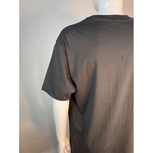 May include: A dark gray t-shirt with short sleeves. The shirt is displayed on a mannequin. The fabric appears to be a soft cotton blend. The shirt's simple design makes it suitable for casual wear.