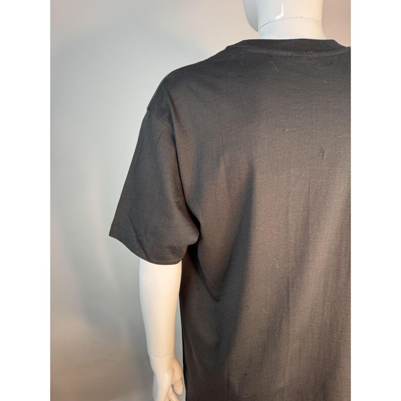 May include: A dark gray t-shirt with short sleeves. The shirt is displayed on a mannequin. The fabric appears to be a soft cotton blend. The shirt's simple design makes it suitable for casual wear.