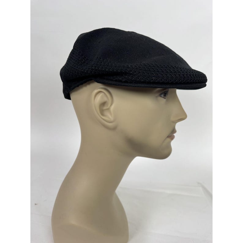 May include: A black newsboy cap with a textured knit design. The cap has a rounded crown and a short, stiff brim. The cap is displayed on a mannequin head.