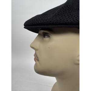 May include: Black newsboy cap with a textured knit design. The cap has a short brim and a rounded crown. The hat is displayed on a mannequin head against a white background. This hat is a classic accessory.