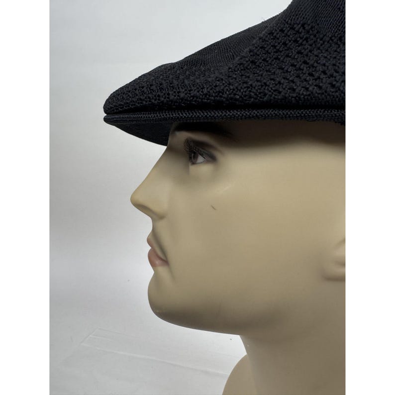 May include: Black newsboy cap with a textured knit design. The cap has a short brim and a rounded crown. The hat is displayed on a mannequin head against a white background. This hat is a classic accessory.