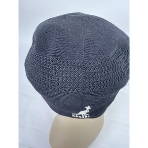 May include: A dark gray, knitted Kangol hat. The hat features a textured knit pattern on the lower portion and a smoother knit on the top. The Kangol logo is embroidered in white on the side. The hat is shown on a mannequin head.