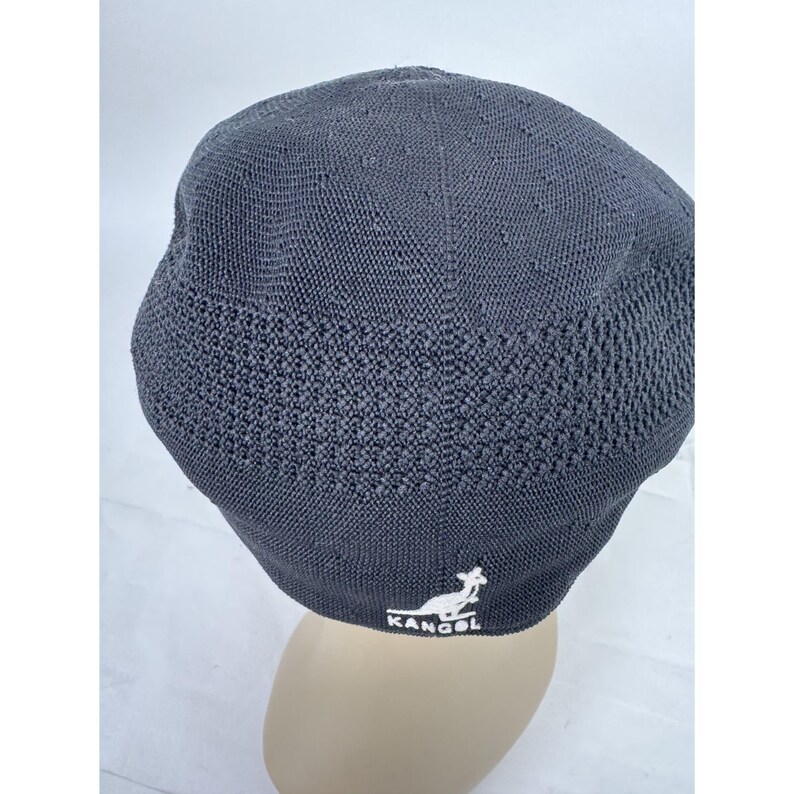 May include: A dark gray, knitted Kangol hat. The hat features a textured knit pattern on the lower portion and a smoother knit on the top. The Kangol logo is embroidered in white on the side. The hat is shown on a mannequin head.