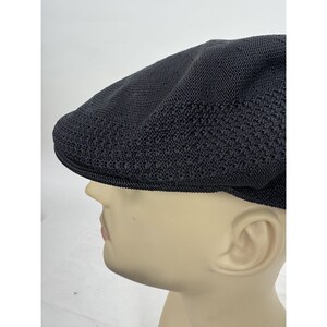 May include: A black, textured flat cap with a rounded crown and a short, stiff brim. The cap is made of a woven material, and it is displayed on a mannequin head. The cap is a classic style, suitable for various occasions.