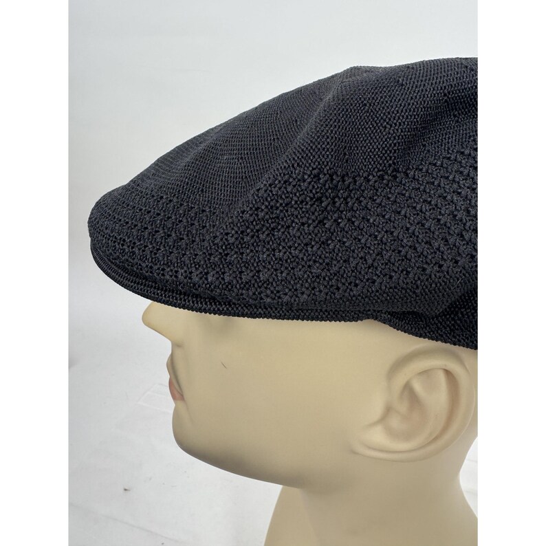 May include: A black, textured flat cap with a rounded crown and a short, stiff brim. The cap is made of a woven material, and it is displayed on a mannequin head. The cap is a classic style, suitable for various occasions.