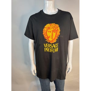May include: Black t-shirt featuring a gold and orange Medusa head graphic with the text "VERSACE PROFUMI" in yellow. The shirt is a classic crew neck style.