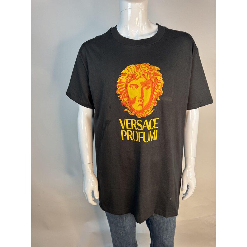 May include: Black t-shirt featuring a gold and orange Medusa head graphic with the text "VERSACE PROFUMI" in yellow. The shirt is a classic crew neck style.