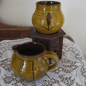 May include: Two brown pottery pieces with a yellow glaze. The larger piece has a stylized flower design and the smaller piece has a striped design.
