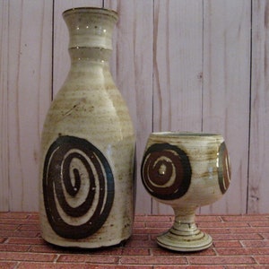 May include: A set of two ceramic pottery pieces, a brown and white bottle and a goblet, both with a swirling brown design.