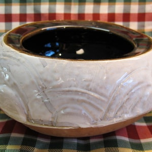 May include: A white ceramic bowl with a brown rim and a textured design. The bowl is empty and has a glossy finish.
