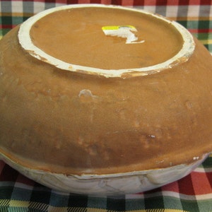 May include: A large, brown ceramic bowl with a white rim. The bowl has a glazed finish and is decorated with a subtle pattern. The bottom of the bowl is visible, showing a brown clay base.