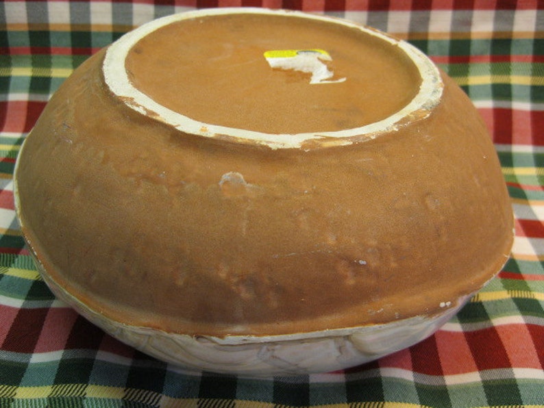 May include: A large, brown ceramic bowl with a white rim. The bowl has a glazed finish and is decorated with a subtle pattern. The bottom of the bowl is visible, showing a brown clay base.