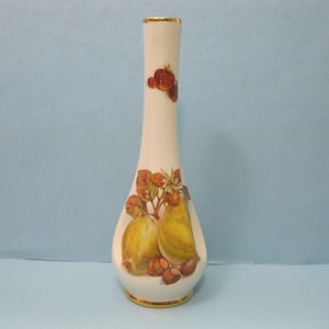 May include: A white ceramic vase with a gold rim and a pear and berry design. The vase is decorated with a pear, leaves, and berries in shades of green, brown, and red.