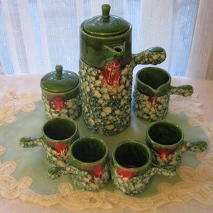 May include: A green and white ceramic tea set with a teapot, creamer, sugar bowl, and four cups. The set has a speckled glaze with red accents.