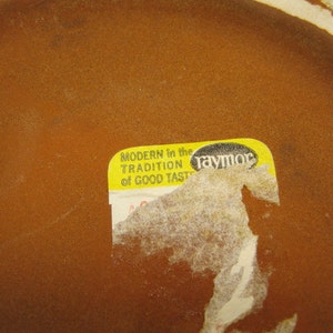 May include: A yellow sticker with the text "MODERN in the TRADITION of GOOD TASTE" and the word "raymor" in black lettering.