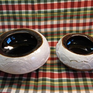 May include: Two ceramic bowls with a white glaze and brown interior. The bowls have a raised design around the rim.