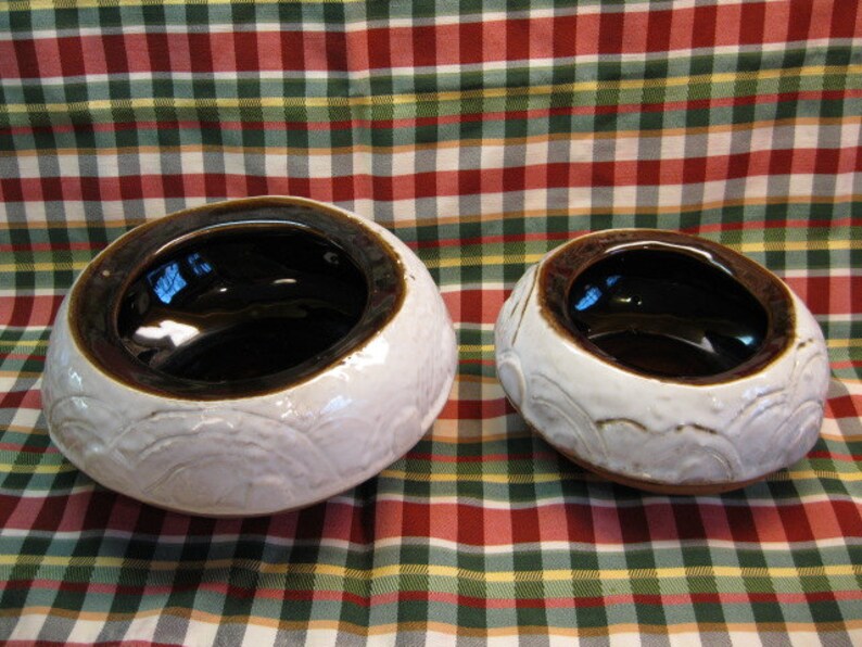 May include: Two ceramic bowls with a white glaze and brown interior. The bowls have a raised design around the rim.