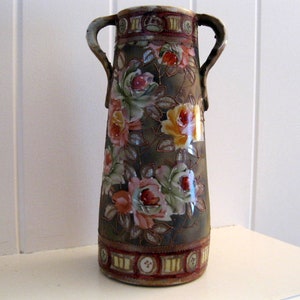 May include: A brown ceramic vase with two handles and a floral design. The vase is decorated with pink, yellow, and white flowers and green leaves. The vase has a gold trim around the top and bottom.