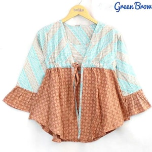 Op de afbeelding: Een patroon top in groen en bruin met een striksluiting. De top heeft een V-hals en driekwart mouwen met een gefranjde zoom. Het hangt aan een houten hanger met "batiku" erop gedrukt. De woorden "Green Brown" staan in de rechterbovenhoek.