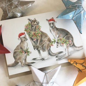 Carte de Noël australienne avec une famille de kangourous, feuille de gomme d'eucalyptus et couronne de fleurs de fleurs d'eucalyptus, chapeaux de père Noël, joli joey, faune australienne