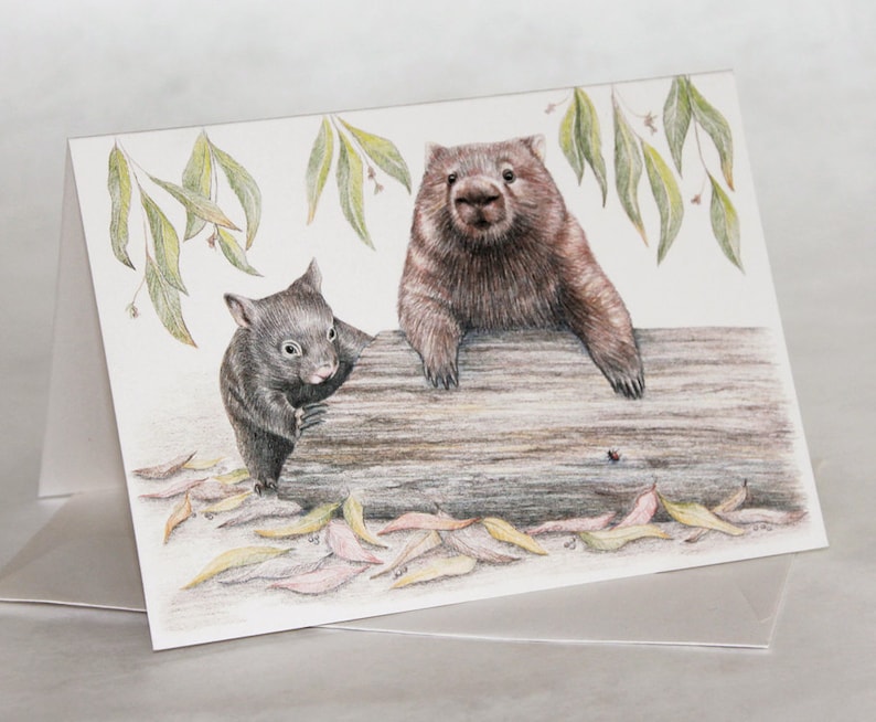 May include: A hand-drawn illustration of two wombats, one adult and one baby, sitting on a log. The adult wombat is brown and has a black nose, while the baby wombat is black. The background is white with green leaves.