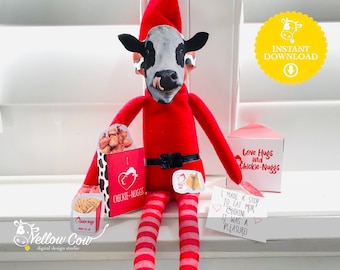 Könnte beinhalten: Ein roter Elf mit einer Kuhmaske hält eine Chick-fil-A-Box mit Chicken Nuggets. Der Elf sitzt auf einer weißen Oberfläche mit einem Schild, auf dem "Love Hugs and Chickie-Nuggs" steht. Es gibt ein weiteres Schild, auf dem "I made a stop to eat mor chikin it was a pleasure!" steht.