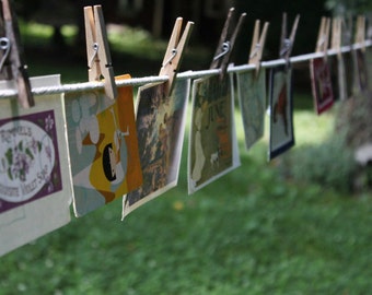 Puede incluir: Un tendedero con varias postales colgadas de pinzas. Las postales presentan diferentes diseños, incluyendo un patrón floral, un diseño geométrico y una escena de paisaje. Las postales son todas en varios tonos de azul, verde, amarillo y rojo.