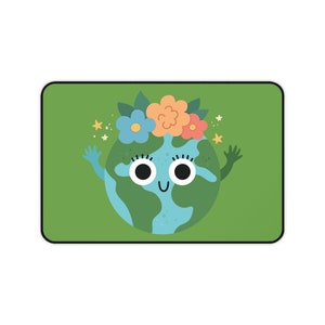 Könnte beinhalten: Ein rechteckiges grünes Mauspad mit einem Cartoon-Erdball mit einem lächelnden Gesicht, blauen und grünen Kontinenten und einem Blumenkranz. Die Erde hat die Arme in einer einladenden Geste erhoben, mit Sternen und Blumen um sie herum.