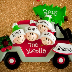 May include: A red and light gray truck Christmas ornament featuring four smiling faces wearing hats labeled Dad, Mom, Carlos, and Karen. A green Christmas tree on top is marked 2016. The side reads The Knolls, and a dog bowl is labeled Roxy.