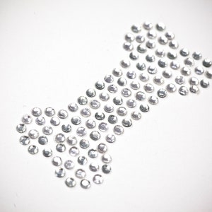 May include: A white bone-shaped design made of small, clear rhinestones.