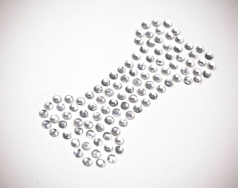 May include: A white bone-shaped design made of small, clear rhinestones.