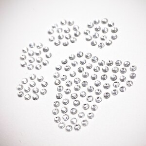 May include: A paw print design made of clear rhinestones on a white background.