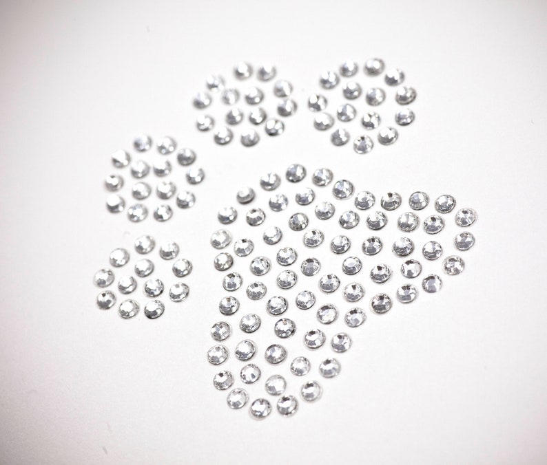 May include: A paw print design made of clear rhinestones on a white background.