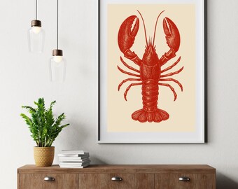 May include: Red lobster illustration art print in a white frame. The lobster is depicted in a vintage style with detailed lines and shading. The background is a light beige color. The print is displayed on a wooden cabinet with a plant and hanging lights.
