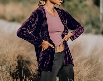 May include: A purple velvet cardigan with long sleeves and a relaxed fit. The cardigan is open in the front and has pockets on the sides.