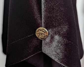 May include: Close-up of a black velvet fabric with a gold button featuring a rose design.