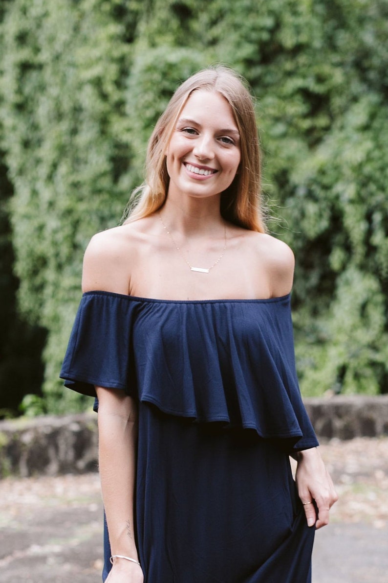 May include: A woman wearing a navy blue off-the-shoulder dress with a ruffled neckline. She is smiling and has long blonde hair.