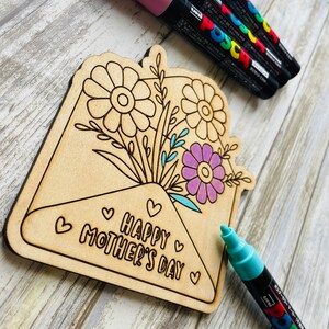May include: Wooden craft project shaped like an envelope with a bouquet of flowers and the text "Happy Mother's Day" inside. The craft is unfinished and ready to be colored with markers.
