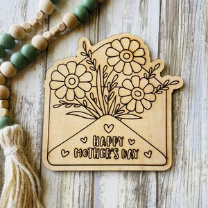 May include: A wooden craft project featuring a floral bouquet inside an envelope with the text "Happy Mother's Day" and hearts.