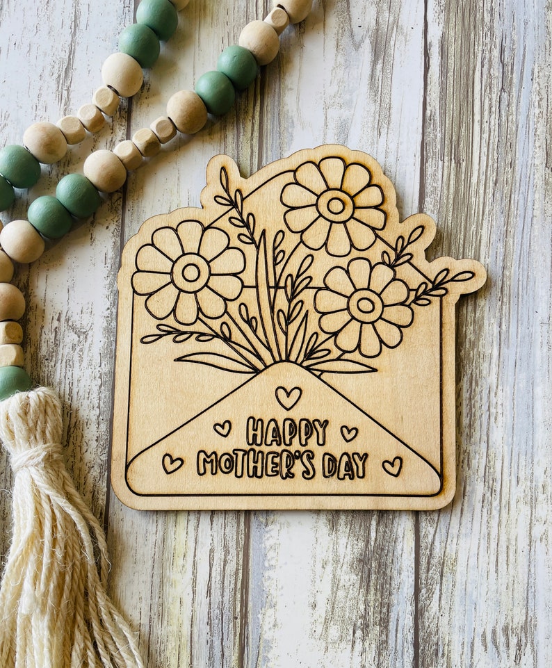 May include: A wooden craft project featuring a floral bouquet inside an envelope with the text "Happy Mother's Day" and hearts.