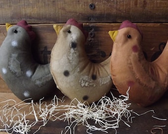 May include: Three handmade fabric chickens in different colors and patterns. The chickens are sitting on a bed of white straw.