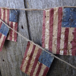 May include: A string of small, faded American flags hanging on a weathered wooden surface. The flags are red, white, and blue with a distressed look.