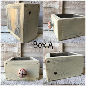 May include: Box A, a rustic wooden box with a distressed, off-white finish. The box features a decorative knob with a colorful pattern. The box is constructed with visible screws and has a square shape. The text "Box A" is visible.