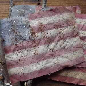 May include: Three American flags made of fabric with a distressed, vintage look. The flags are attached to sticks and have a faded red, white, and blue color scheme.